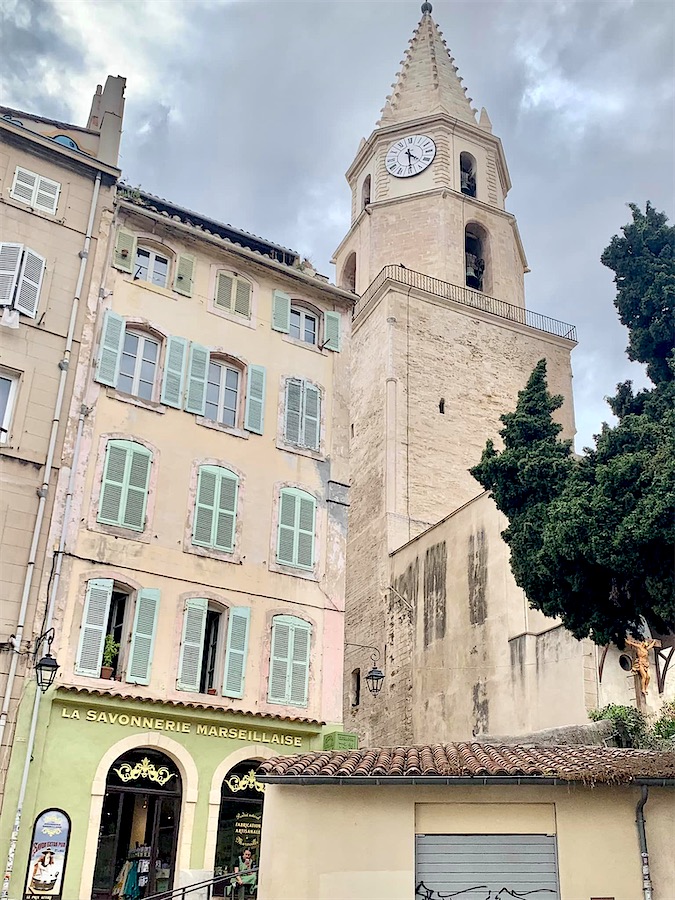 batiment à la façade beige clair et aux volets à persienne vert clair. Au rez-de chaussée, boutique à la façade verte